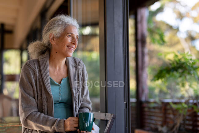 Розслаблююча старша біла жінка на балконі сидить і п'є каву. пенсійний спосіб життя, проводити час наодинці вдома . — стокове фото