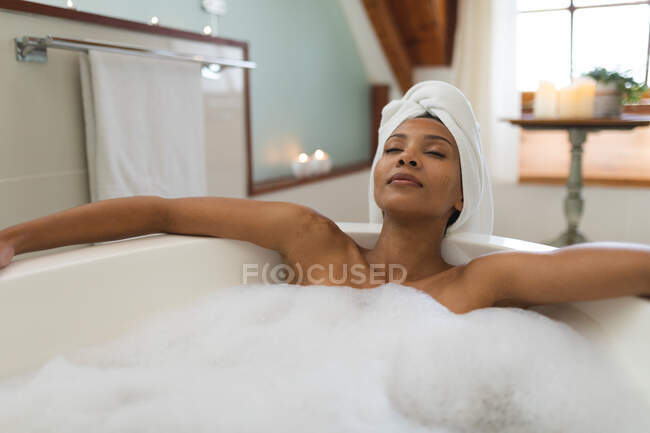 Gemischte Rassenfrau im Badezimmer mit Badewanne, entspannend mit geschlossenen Augen. häuslicher Lebensstil, selbstgepflegte Freizeit zu Hause genießen. — Stockfoto
