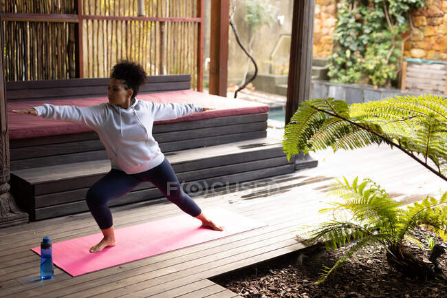 Mulher de raça mista praticando ioga no tapete de ioga com garrafa de água. passar o tempo fora em casa. — Fotografia de Stock