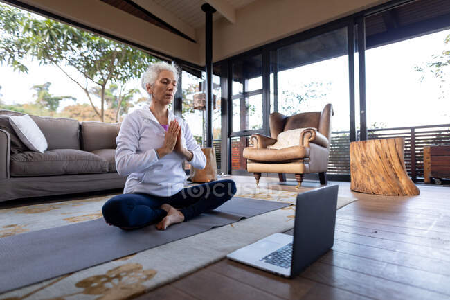 Mulher caucasiana sênior na sala de estar exercitando e meditando, sentada no chão. estilo de vida aposentadoria, passar o tempo sozinho em casa. — Fotografia de Stock