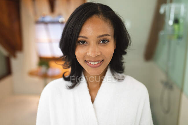 Portrait of smiling mixed race woman in bathroom looking at camera. domestic lifestyle, enjoying self care leisure time at home. — Stock Photo
