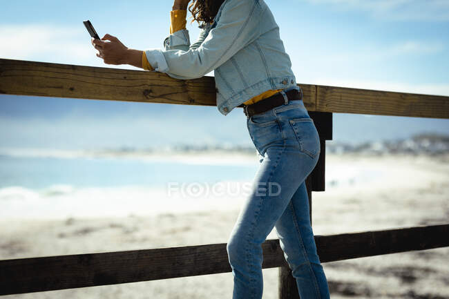 Femme utilisant smartphone le jour ensoleillé au bord de la mer. mode de vie sain, profiter du temps libre à l'extérieur. — Photo de stock