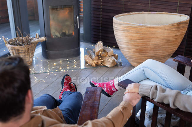 Щаслива різноманітна пара у вітальні, що сидить біля каміна, тримаючись за руки. вихідні вдома в сучасній квартирі . — стокове фото