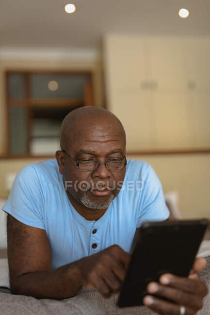 Ein älterer afrikanisch-amerikanischer Mann legt sich ins Bett und benutzt Tabletten. Lebensstil im Ruhestand, Zeit allein zu Hause verbringen. — Stockfoto