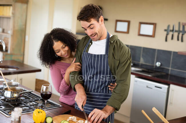 Feliz pareja diversa en la cocina preparando la comida juntos picando verduras. pasar tiempo libre en casa en apartamento moderno. - foto de stock