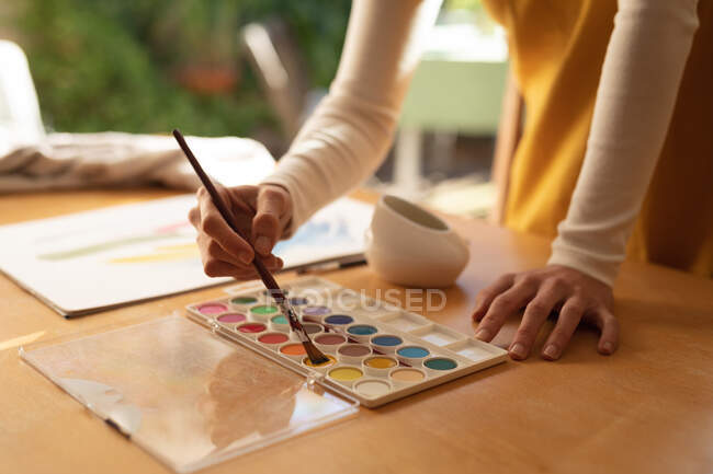 Frau im Wohnzimmer, am Tisch sitzend und malend. häuslicher Lebensstil, Freizeit zu Hause genießen. — Stockfoto