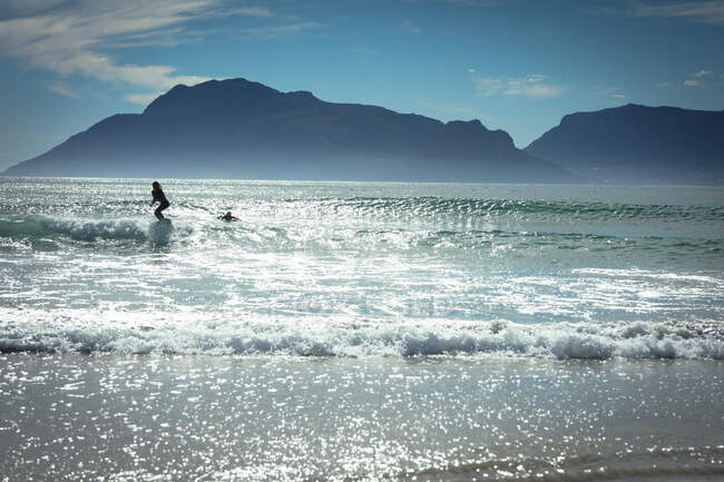 Змішана раса жінка, яка серфінгує в морі в сонячний день. здоровий спосіб життя, насолоджуючись дозвіллям на відкритому повітрі . — стокове фото