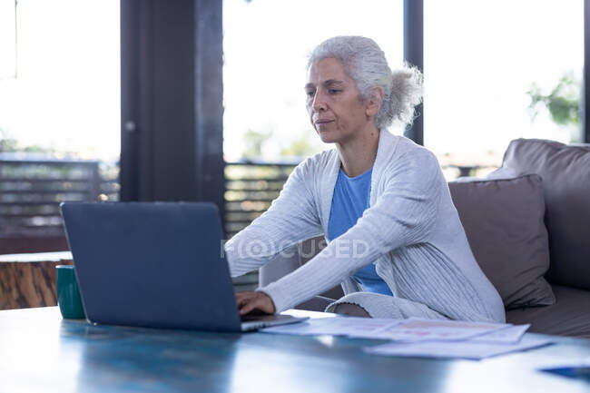 Donna caucasica anziana in soggiorno seduta sul divano, usando il computer portatile. stile di vita di pensione, trascorrere del tempo da solo a casa. — Foto stock