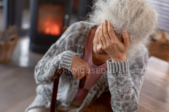 Задумчивая белая женщина, сидящая на кухне, опираясь на трость. пенсионного образа жизни, проводить время в одиночестве на дому. — стоковое фото