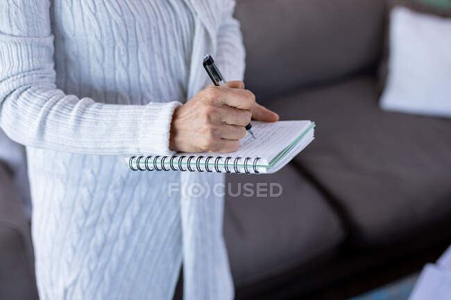 Sezione centrale della donna anziana in soggiorno in piedi e prendere appunti. stile di vita di pensione, trascorrere del tempo da solo a casa. — Foto stock
