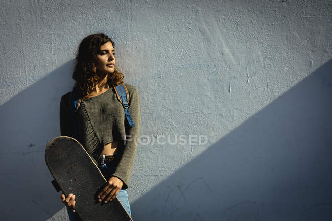 Змішана расова жінка тримає скейтборд у сонячний день на вулиці. здоровий спосіб життя, насолоджуючись дозвіллям на відкритому повітрі . — стокове фото