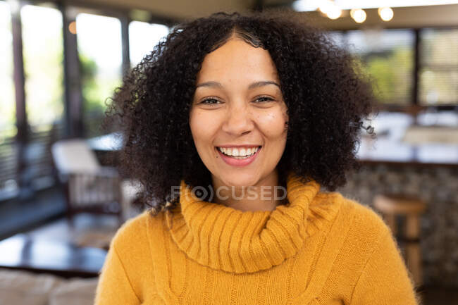 Retrato de la feliz mujer de raza mixta sonriendo y mirando a la cámara. pasar tiempo libre en casa en apartamento moderno. - foto de stock