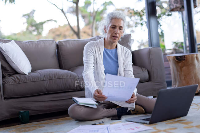 Senior caucasian woman in living room sitting on the floor and using laptop. retirement lifestyle, spending time alone at home. — Stock Photo