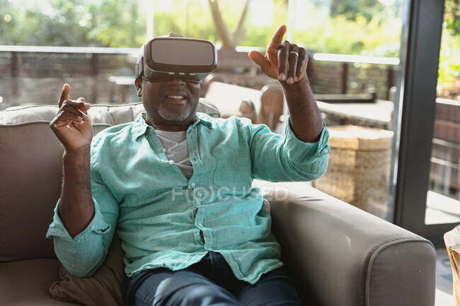 Feliz homem afro-americano sênior sentado e usando headset vr na sala de estar moderna. estilo de vida aposentadoria, passar o tempo sozinho em casa. — Fotografia de Stock
