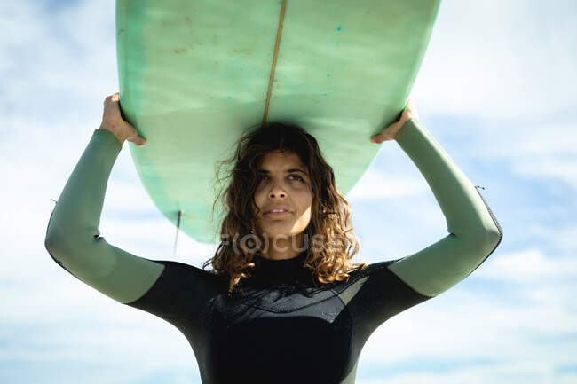 Mixed race woman holding surfboard on sunny day at beach. healthy lifestyle, enjoying leisure time outdoors. — Stock Photo