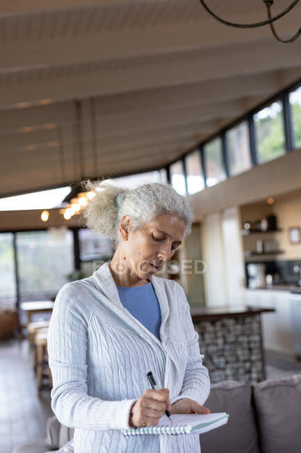Mulher caucasiana sênior na cozinha de pé e fazendo anotações. estilo de vida aposentadoria, passar o tempo sozinho em casa. — Fotografia de Stock