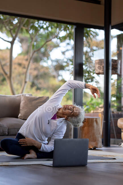 Donna caucasica anziana in salotto che si allena, seduta sul pavimento. stile di vita di pensione, trascorrere del tempo da solo a casa. — Foto stock
