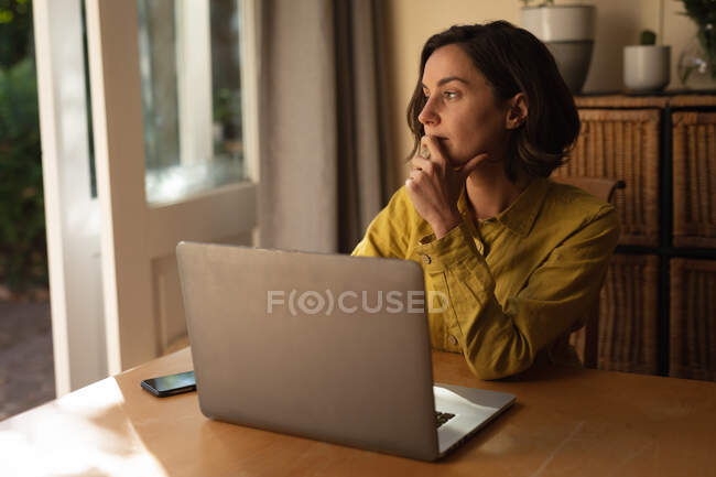Caucasian woman in living room sitting at table, working using laptop. domestic lifestyle, remote working from home. — Stock Photo