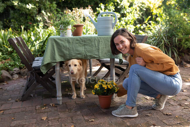 Portrait of smiling caucasian woman in garden with her pet dog, gardening. domestic lifestyle, enjoying leisure time at home. — Stock Photo