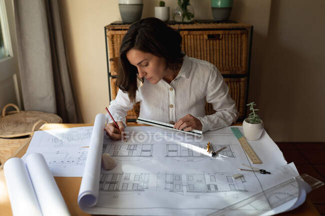 Arquiteta branca na sala de estar, sentada à mesa a trabalhar, a desenhar planos. estilo de vida doméstico, trabalho remoto de casa. — Fotografia de Stock