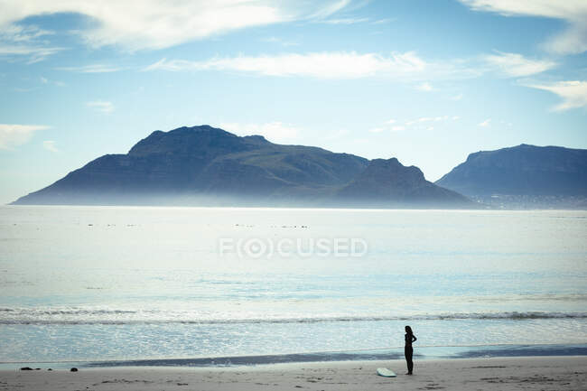 Mixed Race Frau mit Surfbrett am Strand an einem sonnigen Tag. gesunder Lebensstil, Freizeit im Freien genießen. — Stockfoto