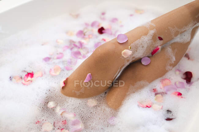 Середня частина жінки у ванній кімнаті з кураторською ванною з червоними та рожевими пелюстками троянд. домашній спосіб життя, насолоджуючись доглядом за дозвіллям вдома . — стокове фото