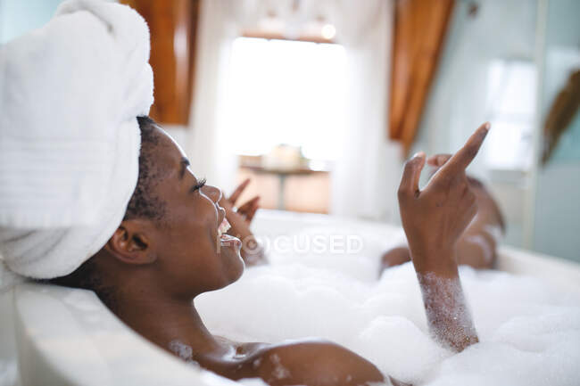 Laughing african american woman in bathroom, relaxing in bath. domestic lifestyle, enjoying self care leisure time at home. — Stock Photo