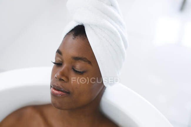 Lächelnde Afroamerikanerin im Badezimmer entspannt sich in der Badewanne mit geschlossenen Augen. häuslicher Lebensstil, selbstgepflegte Freizeit zu Hause genießen. — Stockfoto