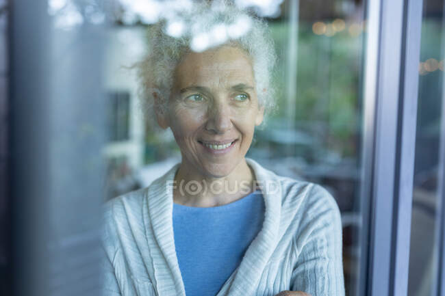 Задумчивая старшая белая женщина в гостиной, смотрит в окно. пенсионного образа жизни, проводить время в одиночестве на дому. — стоковое фото