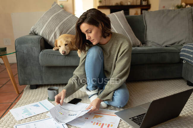 Кавказька жінка з домашнім собакою сидить на підлозі, використовуючи ноутбук. Домашній спосіб життя, дистанційна праця з дому. — стокове фото