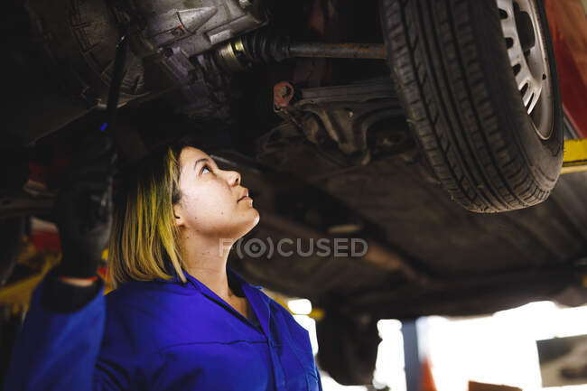 Corrida mista feminino carro mecânico vestindo macacão, inspecionando carro. proprietário de empresa independente na garagem de manutenção de carro. — Fotografia de Stock