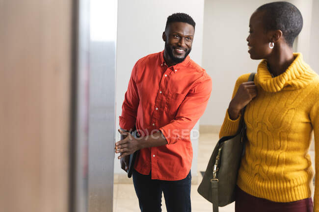 Sorrindo afro-americanos colegas criativos masculinos e femininos conversando no elevador. pessoas de negócios criativas independentes em um escritório moderno. — Fotografia de Stock