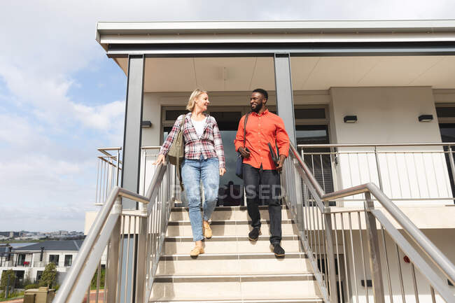 Smiling diverse female and male colleagues walking downstairs outside office and talking. independent creative business people at a modern office. — Stock Photo