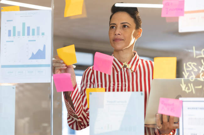 Serious caucasian female business creative brainstorming and writing memo notes on glass wall. independent creative business people working at a modern office. — Stock Photo