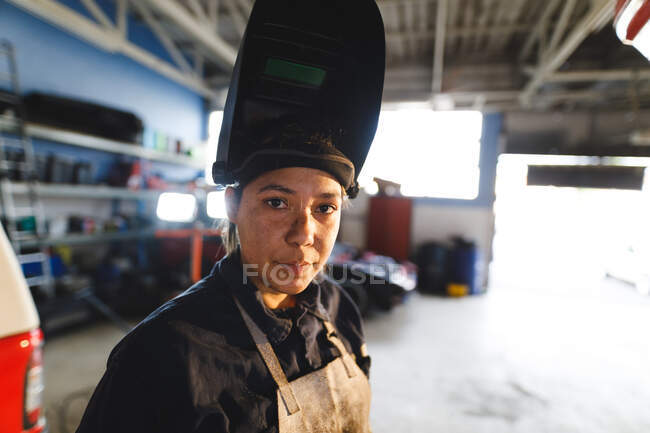 Mixed Race Automechanikerin in Overalls und Schweißmaske, blickt in die Kamera. Selbstständiger Unternehmer in der Kfz-Werkstatt. — Stockfoto