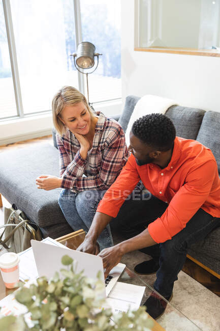 Sonriendo diversos colegas femeninos y masculinos sentados en el sofá en la sala de estar del lugar de trabajo y utilizando el ordenador portátil. empresarios creativos independientes en una oficina moderna. - foto de stock