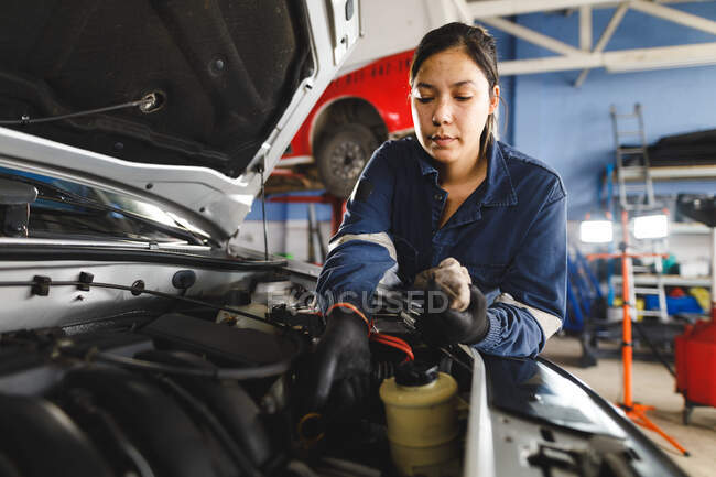 Corrida mista feminino carro mecânico vestindo macacão, verificando o nível de óleo. proprietário de empresa independente na garagem de manutenção de carro. — Fotografia de Stock