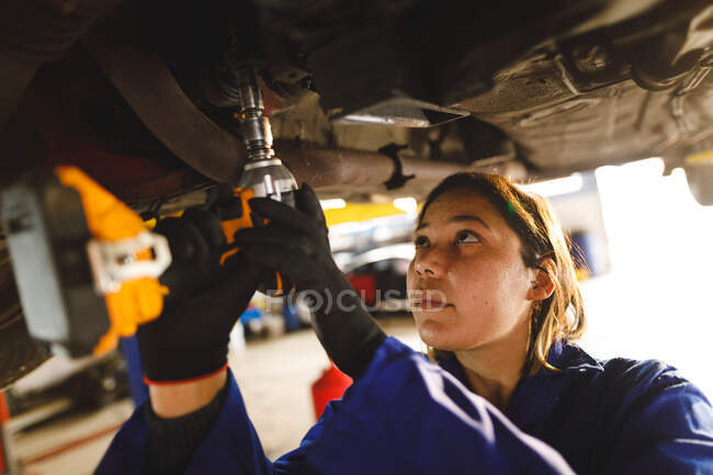 Mixed race female car mechanic wearing overalls, using screwdriver. independent business owner at car servicing garage. — Stock Photo