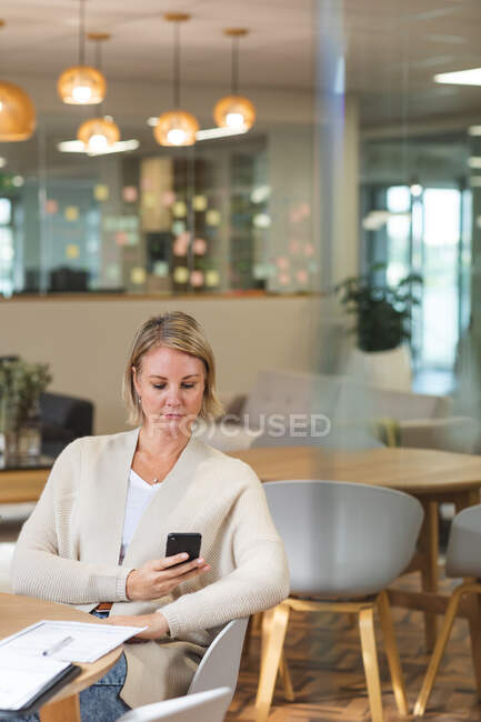 Thoughtful caucasian female business creative using smartphone at workplace cafeteria. independent creative business people working at a modern office. — Stock Photo