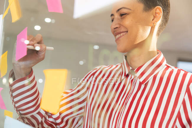 Sorridente caucasico business femminile creativo brainstorming e la scrittura di appunti memo sulla parete di vetro. uomini d'affari creativi indipendenti che lavorano in un ufficio moderno. — Foto stock