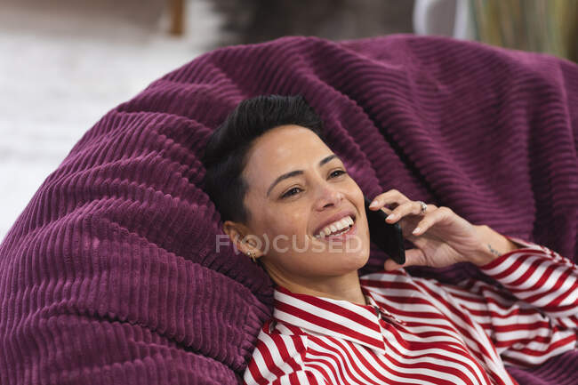 Улыбающаяся кавказка-деловая креативщица лежит на диване и пользуется смартфоном. независимые креативные бизнесмены, работающие в современном офисе. — стоковое фото
