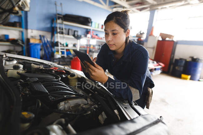 Misto gara femminile meccanico di auto che indossa tuta intera, ispezionare auto, utilizzando tablet. proprietario indipendente presso il garage di assistenza auto. — Foto stock