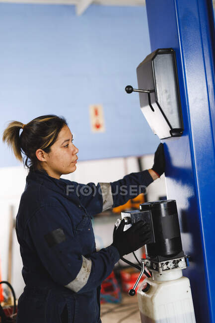 Mixed race female car mechanic wearing overalls, using tools. independent business owner at car servicing garage. — Stock Photo