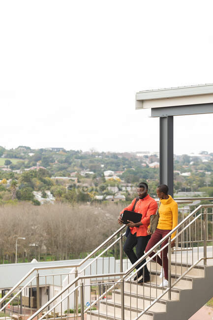 Lächelnde afrikanisch-amerikanische Kreativ-Kolleginnen gehen die Treppe hinunter und unterhalten sich. Unabhängige kreative Geschäftsleute in einem modernen Büro. — Stockfoto