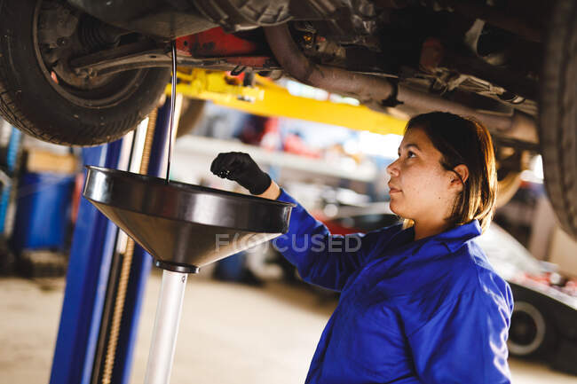 Corrida mista feminino carro mecânico vestindo macacão, verificando o nível de óleo. proprietário de empresa independente na garagem de manutenção de carro. — Fotografia de Stock