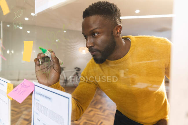 Seriöse afrikanisch-amerikanische männliche Business kreatives Brainstorming und Schreiben von Memo-Notizen auf Glaswand. unabhängige kreative Geschäftsleute, die in einem modernen Büro arbeiten. — Stockfoto