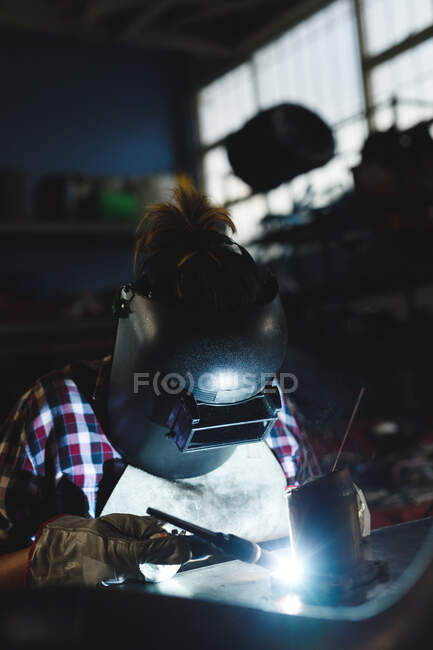 Mixed race female car mechanic welding car part in workshop. independent business owner at car servicing garage. — Stock Photo
