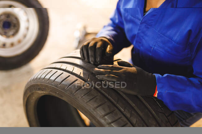 Mittelteil einer Automechanikerin, die Overalls trägt und Reifen kontrolliert. Selbstständiger Unternehmer in der Kfz-Werkstatt. — Stockfoto