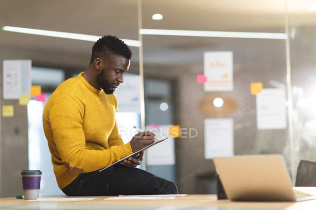 Serious african american male business creative sitting on desk and making notes. independent creative business people working at a modern office. — Stock Photo