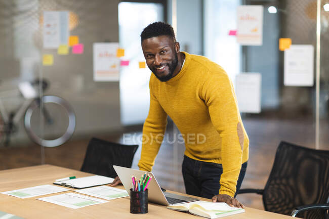 Lächelnd steht ein amerikanischer Geschäftsmann am Schreibtisch und blickt in die Kamera. unabhängige kreative Geschäftsleute, die in einem modernen Büro arbeiten. — Stockfoto